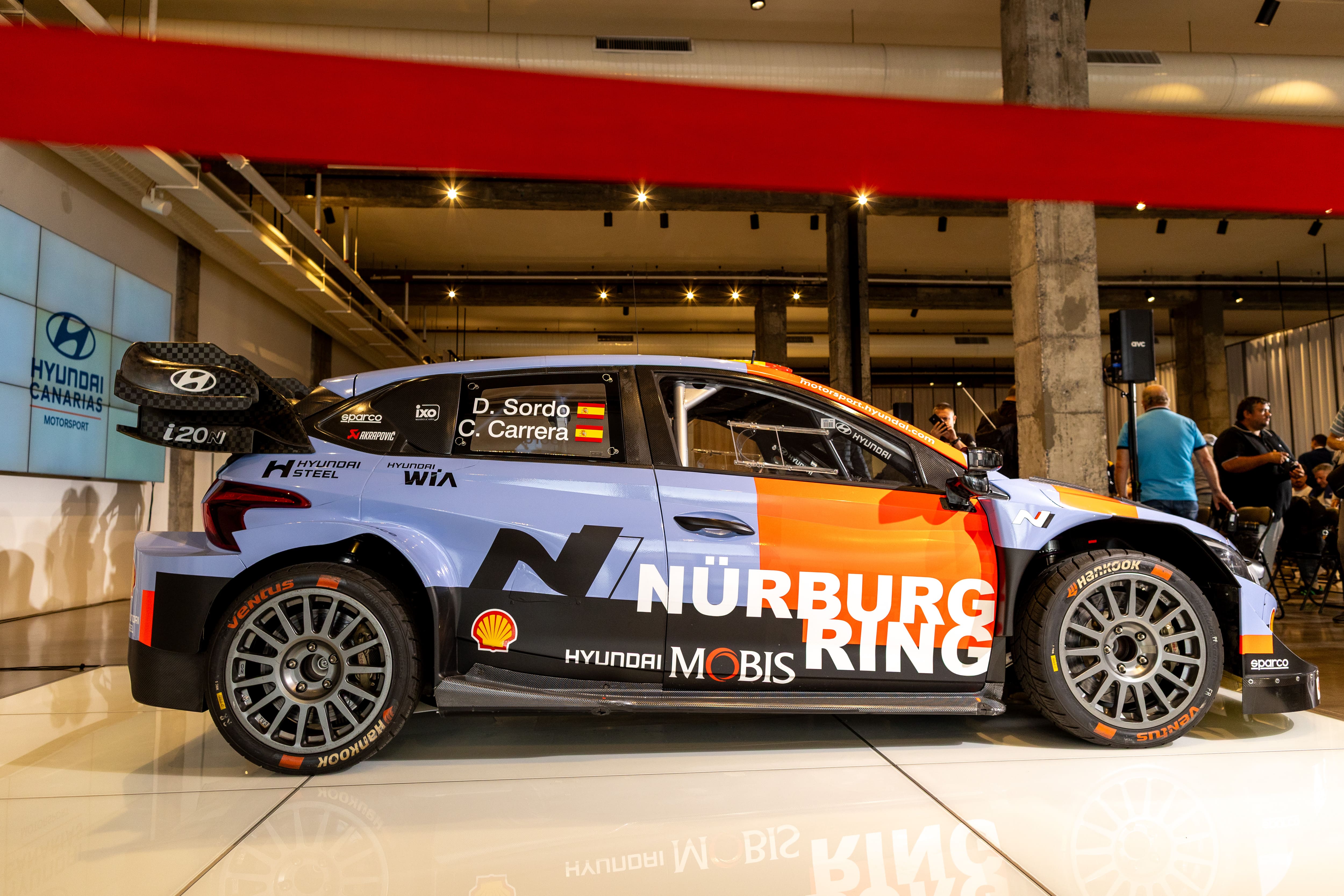 Vista lateral de un coche de rally Hyundai i20 N Rally1 con los nombres de los pilotos D. Sordo y C. Carrera en la ventanilla.